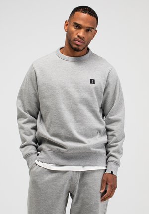 Grijze crewneck trui van zacht materiaal, met geribbelde manchetten en zoom, en een klein zwart logo aan de voorkant.