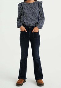 Marinblus med vita prickar, puffärmar och dekorativa s ömmar, i kombination med mörk denimbucken jeans och bruna ankelstövlar.