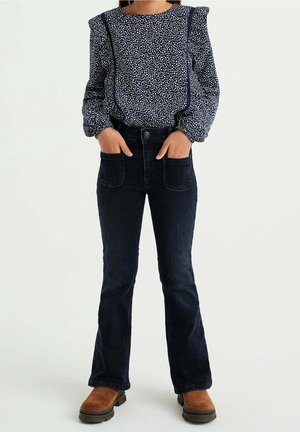 Marinblus med vita prickar, puffärmar och dekorativa sömmar, i kombination med mörk denimbucken jeans och bruna ankelstövlar.