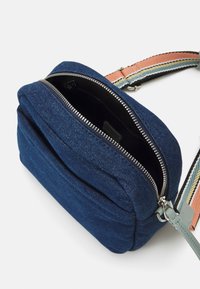 Petit sac d'épaule en tissu bleu avec une fermeture éclair argentée partiellement ouverte et une sangle réglable rayée orange, verte et beige.