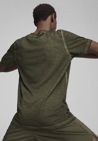 Camiseta deportiva de color verde oliva con mangas cortas, tela texturizada y cuello redondo. Presenta costuras planas y un ajuste relajado.