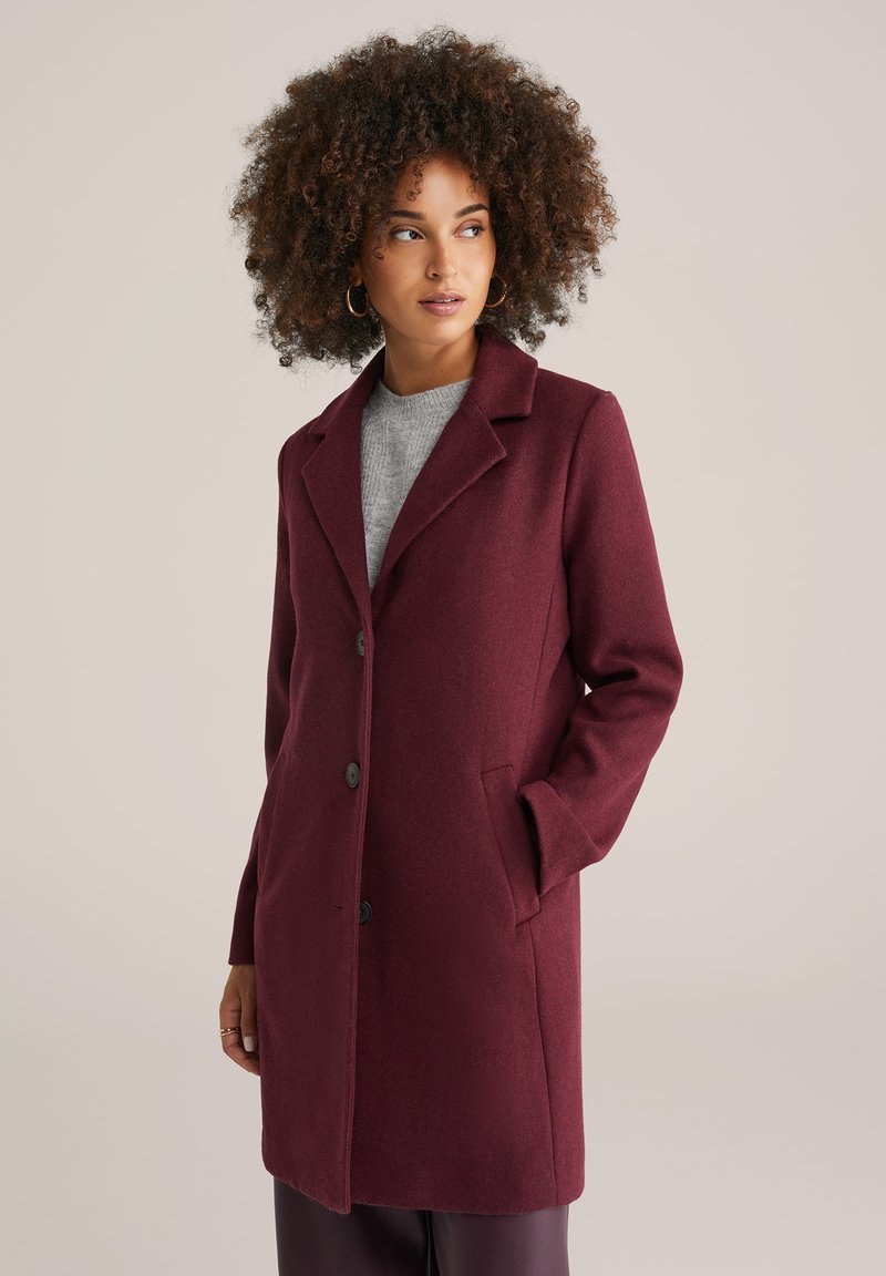 Cappotto in misto lana bordeaux con colletto a punte, tre bottoni, tasche laterali e taglio dritto. Texture liscia e design sartoriale.