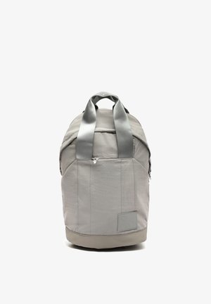 Helehall seljakott kahe käepideme, esikülje tõmblukuga tasku ja alumise parempoolse ristkülikukujulise plaastriga, püstiasendis valgel taustal.