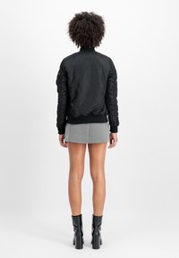 Black padded bomber jacket with ribbed cuffs and hem, featuring a high collar and a smooth texture. Worn over a gray pleated skirt.
