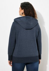 Felpa con cappuccio blu navy, dotata di cucitura posteriore e polsini a costine. Presenta un delicato dettaglio logo sul cappuccio e un design di taglio rilassato.