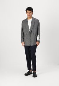 Sacou gri cu carouri, cu design cu două rânduri de nasturi, purtat peste un tricou alb, asortat cu pantaloni negri și mocasini negri.