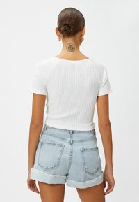 Witte geribbelde top met korte mouwen gecombineerd met lichtblauwe versleten denim shorts met opgerolde manchetten en achterzakken.