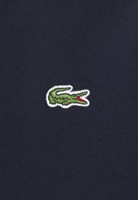 Tessuto di cotone blu navy con una finitura testurizzata, caratterizzato da un piccolo logo di un coccodrillo verde ricamato con accenti rossi.