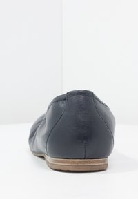 Svart läder platt sko med rund tå, slät textur, subtila sömdetaljer och en ljusbrun sula. Bakvy utan dekorationer.