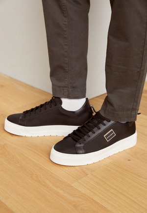 Zapatillas marrones con materiales de malla y cuero, suela de goma blanca, punta redonda, cordones planos y una pequeña etiqueta de marca en el lado.