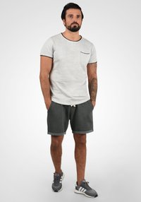T-shirt grise avec des bordures noires et une poche, associé à un short gris foncé avec des ourlets roulés. Porté avec des baskets grises.