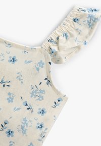 Blomsterpræget top med blødt, cremegult stof, prydet med lyseblå blomster. Designet inkluderer en flæset skulderstrop med elastisk samling.
