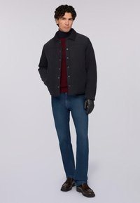 Giacca trapuntata scura con colletto, maglione bordeaux sotto, jeans blu, guanti neri e scarpe marroni. Tessuto strutturato e design aderente.