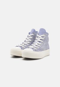 Zapatillas altas de ante en color morado claro con cordones blancos, una superficie texturizada y una gruesa suela de goma blanca. Presentan un diseño de puntera redondeada.