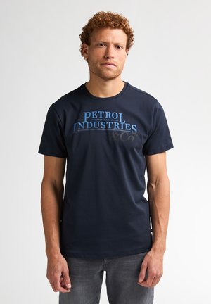 Donkerblauwe katoenen t-shirt met de tekst "PETROL INDUSTRIES" in lichtblauw. Korte mouwen, ronde hals, gladde textuur, casual pasvorm.