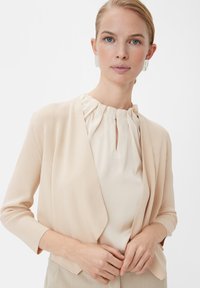 Pfirsichfarbener Cardigan mit weicher Textur, offener Vorderseite und Dreiviertelärmel, kombiniert mit einer cremefarbenen Bluse mit gefälteltem Ausschnitt.