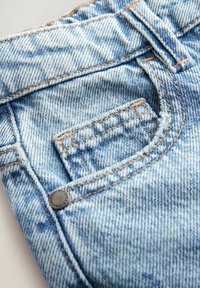 Jeans in denim blu chiaro con tasca frontale, cuciture visibili e un bottone metallico come dettaglio. La texture è in denim classico con un aspetto invecchiato.