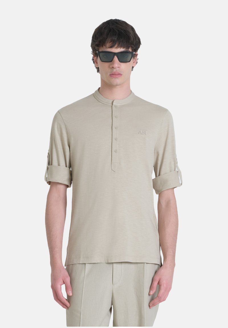 Camicia henley color beige chiaro con colletto rotondo, abbottonatura e maniche arrotolate. Presenta un delicato logo ricamato sul petto.
