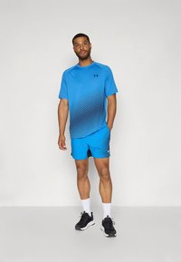 Camisola atlética azul com riscas náuticas em degradê, combinada com calções azuis correspondentes com padrão texturizado. Calçado atlético preto usado.