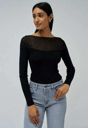 Top negro de manga larga con escote de malla transparente negra y detalles de cuentas, combinado con jeans de tiro alto en gris claro.