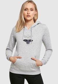 Grå hoodie med v-ringad design, dragsko, framficka och en fjärilsdesign på bröstet. Tillverkad av mjukt tyg med en slät textur.