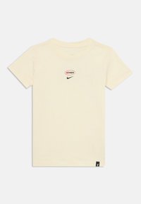 T-shirt en coton crème avec un col rond, arborant un logo "aimax" rouge et noir et un swoosh Nike noir sur le devant.