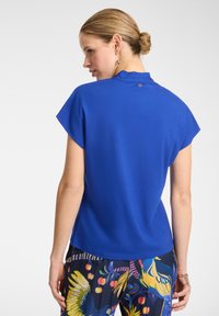Top corto blu royal con scollo scallop e un piccolo dettaglio metallico sul retro, abbinato a pantaloni colorati con fantasia.