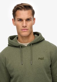 Oliven grøn hoodie lavet af blødt stof, med hætte og snøre, et logo på brystet og en afslappet pasform. Glat tekstur og ingen mønstre.
