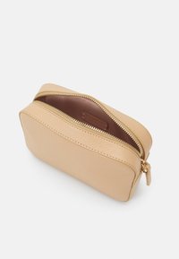 Mała beżowa skórzana saszetka z złotym zamkiem błyskawicznym, częściowo otwarta, odsłaniająca miękkie różowe wnętrze i metkę marki w środku.