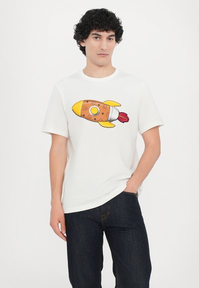 White t-shirt featuring a colorful rocket ship design with a brown body, yellow accents, and red flames, paired with dark jeans.