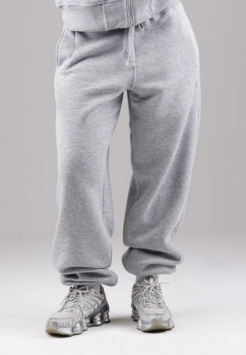 Gray sweatpants with drawstring pockets worn with gray and silver athletic shoes on a gray background.