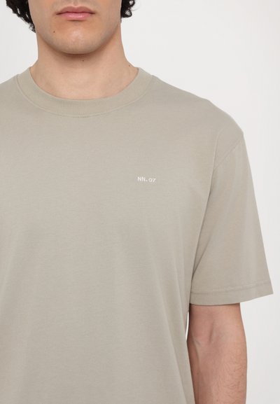 Lichtgrijs katoenen T-shirt met een ronde halslijn en korte mouwen; heeft een kleine witte opdruk "NN. 07" op de linkerborst.