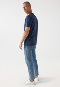 Námořnická modrá bavlněná tričko s kulatým výstřihem, kombinováno se světle modrými zúženými džínami a bílými teniskami. Tkanina vypadá hladce a má uvolněný střih.