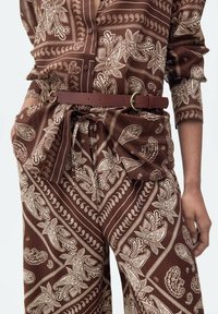 Brown patterned outfit featuring paisley designs; made of lightweight fabric with a button-down shirt and belted, loose-fit trousers.