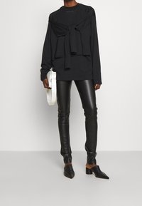 Černý top s dlouhým rukávem a mašlí na výstřihu, kombinovaný s černými slim fit koženými kalhotami a černobílými špičatými botami. Bílá crossbody kabelka.
