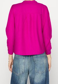Fuchsia, textuur blouse met een relaxed fit, ronde halslijn en elastische manchetten, gecombineerd met blauwe, hoge taille denim jeans.