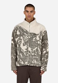 Polarowa kurtka z zamkiem błyskawicznym, w szaro-białym, teksturowanym wzorze. Posiada wysoki kołnierz i centralny zamek. Miękki, ciepły materiał.