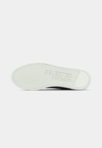 Hvit gummisåle på en sneakers som viser teksturert grep og preget "SELECTED / HOMME"-merke, merket med europeisk størrelse 45.