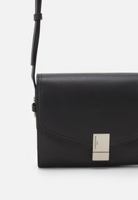 Černá kožená crossbody taška s hladkou texturou, obdélníkovým tvarem a stříbrným obdélníkovým zapínáním se jménem značky.