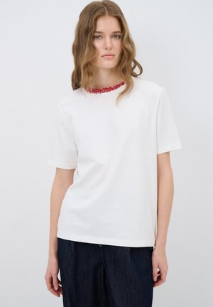T-shirt bianco a maniche corte con colletto decorato da perline rosse. Realizzato in un tessuto liscio, presenta una vestibilità comoda e una texture sottile.