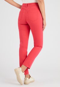 Felroze, strakke broek met een gladde textuur, vijf zakken en een middelhoge taille, gecombineerd met lichtgekleurde sneakers.