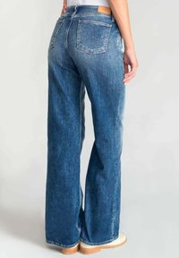 Wijdvallende blauwe spijkerbroek met een vervaagde wassing, voorzien van een middellange taille, twee achterzakken en een leren merkopdruk op de achterkant.