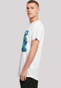 White cotton t-shirt featuring a graphic of a blue monster in a varsity jacket, with a relaxed fit and short sleeves.