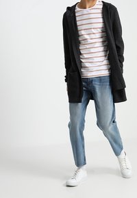 Schwarze kapuzenstrickjacke mit Taschen, getragen über einem weiß-braun gestreiften T-Shirt, kombiniert mit hellblauen Jeans und weißen Sneakers.