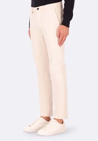 Chinos beige slim fit in twill di cotone, con tasche frontali, chiusura con bottone e linee pulite abbinate a sneaker bianche.