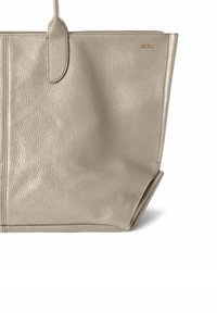 Beige læder tote taske med struktureret finish, der har dobbelte håndtag og en guld logo accent, designet til rummelig opbevaring.