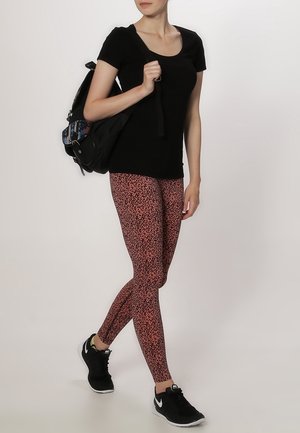 Black short-sleeve top paired with pink and black patterned leggings. Wears black sneakers and carries a black backpack.