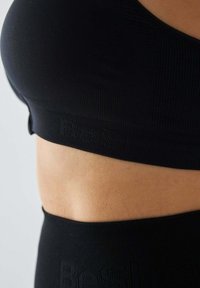 Czarny sportowy bratop z prążkowaną fakturą. Charakteryzuje się bezszwowym designem oraz elastyczną taśmą z wytłoczonym nazwą marki.