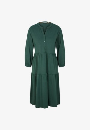 Mujer que lleva un vestido azul oscuro de manga larga hasta la rodilla con escote abotonado y botas de combate negras con cordones.