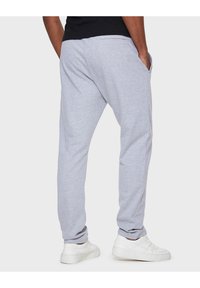Grijze katoenen joggers met een relaxte pasvorm, zijzakken en geribde enkelmanchetten, gecombineerd met witte sneakers op een effen achtergrond.
